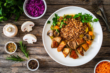 Roast pork with buckwheat groats, mushrooms and carrots served on wooden table
 - obrazy, fototapety, plakaty