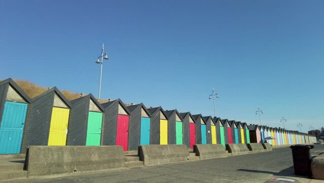 Panning shot of colourful beach huts on the promenade and the sandy beach in the seaside town of Lowestoft. Captured on a bright and sunny morning