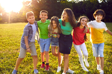 Group of cheerful little kids playing in the park, enjoying summer and having fun together. Bunch of happy friends hugging each other and walking on green sunny meadow. Children, friendship concept