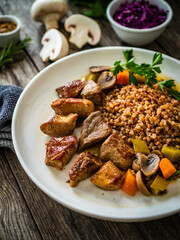 Roast pork with buckwheat groats, mushrooms and carrots served on wooden table
