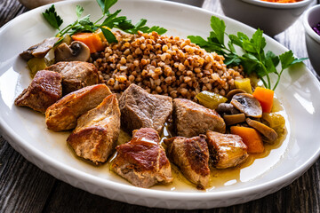 Roast pork with buckwheat groats, mushrooms and carrots served on wooden table
