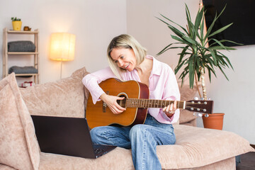 Middle aged woman practicing and learning how to play guitar on laptop