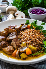 Roast pork with buckwheat groats, mushrooms and carrots served on wooden table
