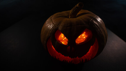 A creepy pumpkin with a carved grimace glows. Jack on a lantern in the dark.