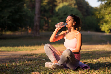 Fototapeta premium Young woman resting and drinking water after exercise in the summer nature