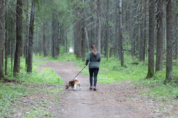 A woman with a dog runs around the summer park. Fitness classes on the street.