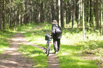 An elderly man, a pensioner, rides a bicycle in a summer park.