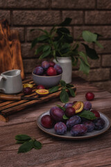 Summer still life with fruits. Rustic still life. Ripe plums on a ceramic plate and a wooden background.