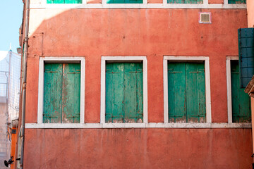 Fototapeta na wymiar red facade with three weathered green window