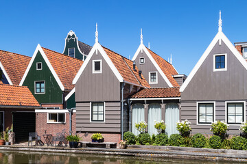 Typical narrow wooden houses with gabled gables and red roof tiles along the river in the Dutch picturesque village of De Rijp in the Beemster.