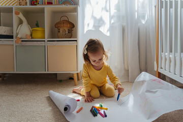 A little girl drawing on floor on paper in the kids room. Educational game for baby and toddler in modern nursery. Early development.