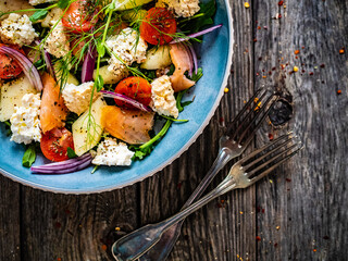 Salmon salad - smoked salmon, white smoked cheese and fresh vegetables on wooden table
