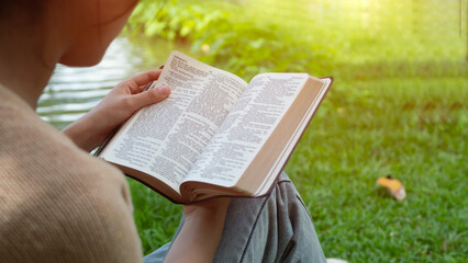 Naklejka premium Christian girl holds bible in her hands. Reading the Holy Bible in a field during beautiful sunset. Concept for faith, spirituality and religion. Peace, hope