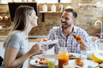 Fototapeta na wymiar Happy young couple talking while enjoying in their breakfast at home