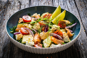Salmon salad - smoked salmon, white smoked cheese and fresh vegetables on wooden table
