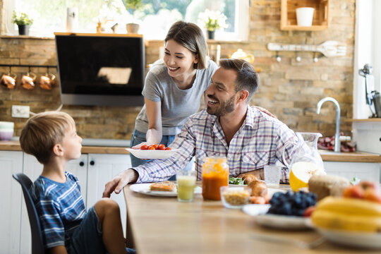 Happy mother serving food to her family while father and son having fun in dining room