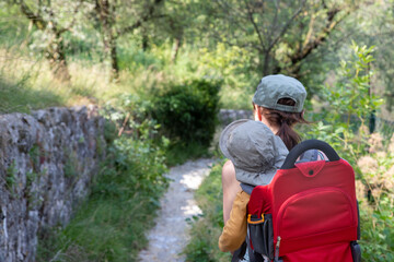 Fototapeta premium Family hiking in the Dolomites, Italy. Young mother is carrying her child in a hiking carrier on a trail