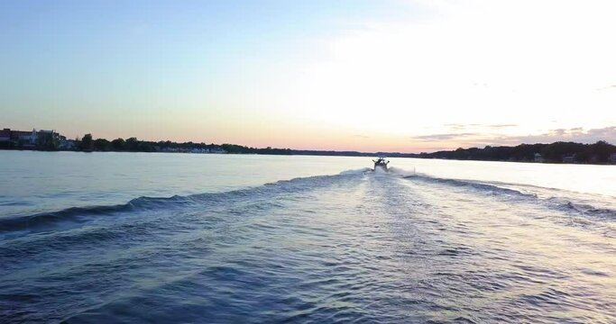 Aerial: Male Tourist Doing Stunts While Surfboarding Behind Speedboat, Drone Flying Forward During Sunset - West Bloomfield, Michigan
