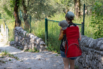 Family hiking in the Dolomites, Italy. Young mother is carrying her child in a hiking carrier on a trail