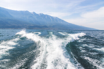 Boat tour: Boat bow, view over azure blue water and mountain range. Lago di Garda, Italy