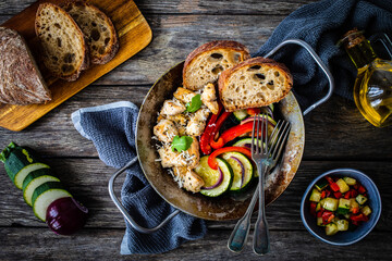 Fried chicken nuggets with bread and vegetables in frying pan on wooden table
