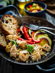 Fried chicken nuggets with bread and vegetables in frying pan on wooden table
