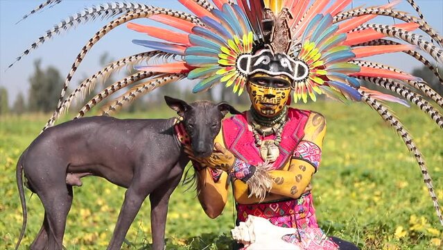 mexican man in prehispanic dancer costume for day of the dead celebration with dog xoloitzcuintle