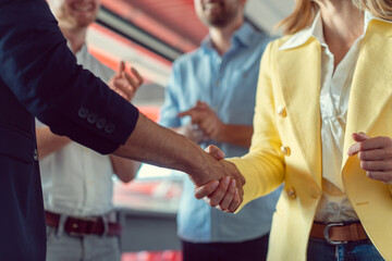 Closing of a business deal by shaking hands in agreement, team applauding in the background
