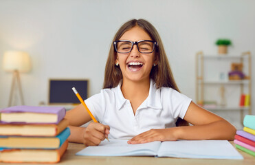Happy, positive child having fun while doing school homework. Portrait of a cheerful student girl...
