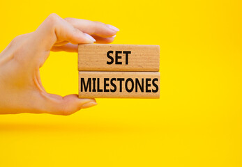 Set milestones symbol. Concept word Set milestones on wooden blocks. Beautiful yellow background. Businessman hand. Business and Set milestones concept. Copy space