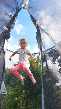 Little girl jumps on a trampoline. Country house. Garden plot. Unbridled fun