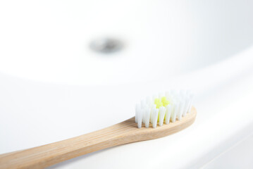 Ecological bamboo toothbrush on the edge of a white sink. Concepts: sustainable lifestyle, use of compostable and environmentally friendly materials, zero plastics. Clear image with copy space.