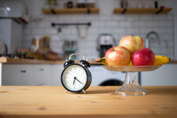 vintage alarm clock and fresh fruit on kitchen table intermittent fasting