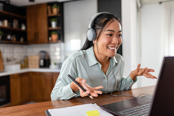 Young Asian women attending online foreign language classes. Sitting in front of a laptop computer with headphones listening to courses and taking notes.