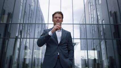 Portrait smiling businessman drinking coffee standing at glass office building.