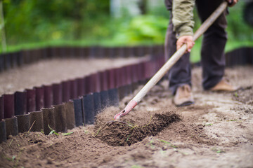 Farmer cultivating land in the garden with hand tools. Soil loosening. Gardening concept....