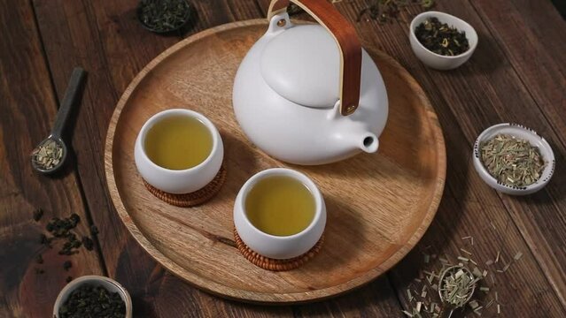 Ceramic white teapot and cups. Dried various kinds of tea on ceramic spoons. Wooden background with copy space