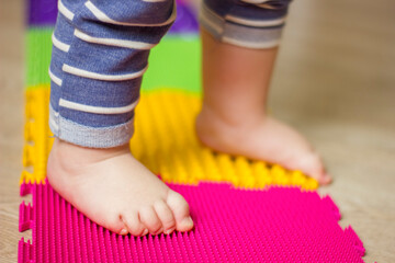 Toddler babye's feet on orthopedic massage mat. Baby foot massage. Exercises for legs on carpet.
