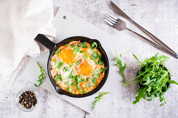 Shakshuka with tomatoes and arugula in a pan. Traditional mediterranean dish. Top view