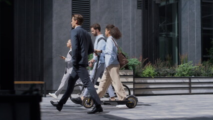 Corporate people walking holding bicycle kickscooter downtown. Green transport.