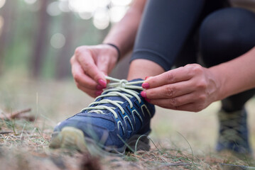 girl soprtsman sits on the pavement and ties shoelaces on sneakers in forest