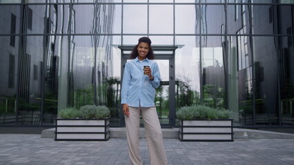 Pleased businesswoman posing drinking coffee cup on contemporary office facade.