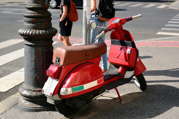 Popular brand Italian made red, white and green scooter closeup at street corner. city and urban transportation concept. asphalt pavement. white pedestrian crossing. young woman and man - Powered by Adobe