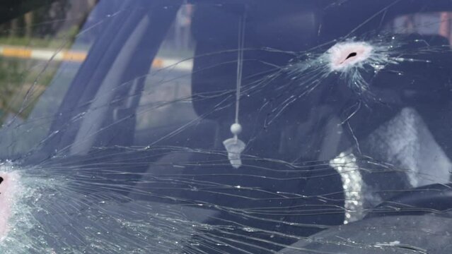 Holes on the windshield of the car, it was shot from a firearm. Bullet holes. Smash car windshield, broken and damaged car. The bullet made a cracked hole in the glass.
