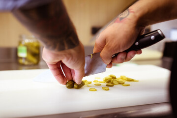 Obraz na płótnie Canvas Partial view of tattooed cook cutting marinated cucumbers in cafe 