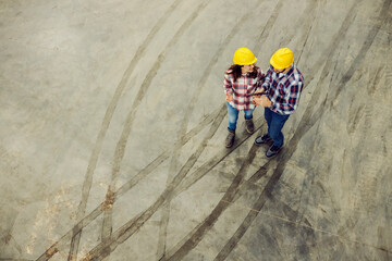 Aerial view of two smiling factory workers walking around facility and talking about business.