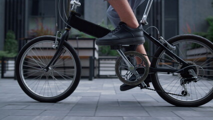 Fototapeta na wymiar Closeup worker legs pedaling at downtown district. Eco-friendly transportation.