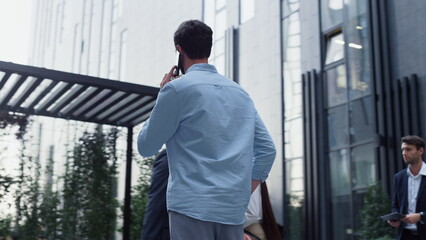 Fototapeta premium Confident man speaking phone at downtown area. Various corporate people walking.