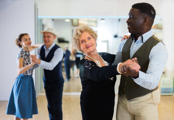 Fototapeta na wymiar Elderly woman learning ballroom dancing in pair in dance studio