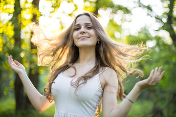 Beautiful young Russian girl dressed in a white dress, walks through the forest among the oaks in the rays of the sunset